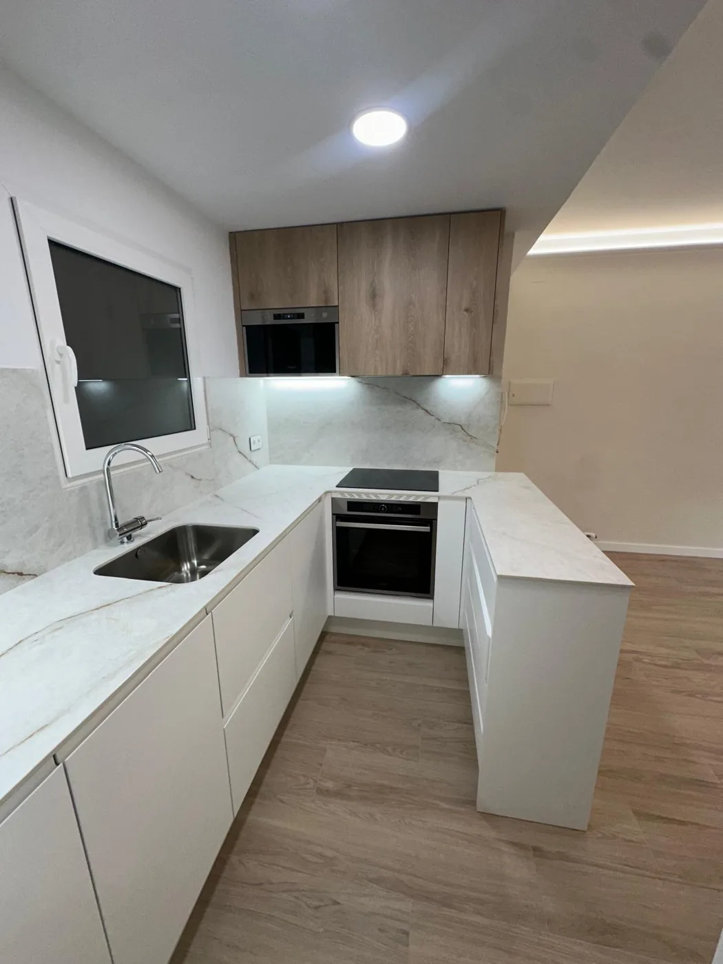 Cocina blanca y de madera con horno integrado y encimera veteada