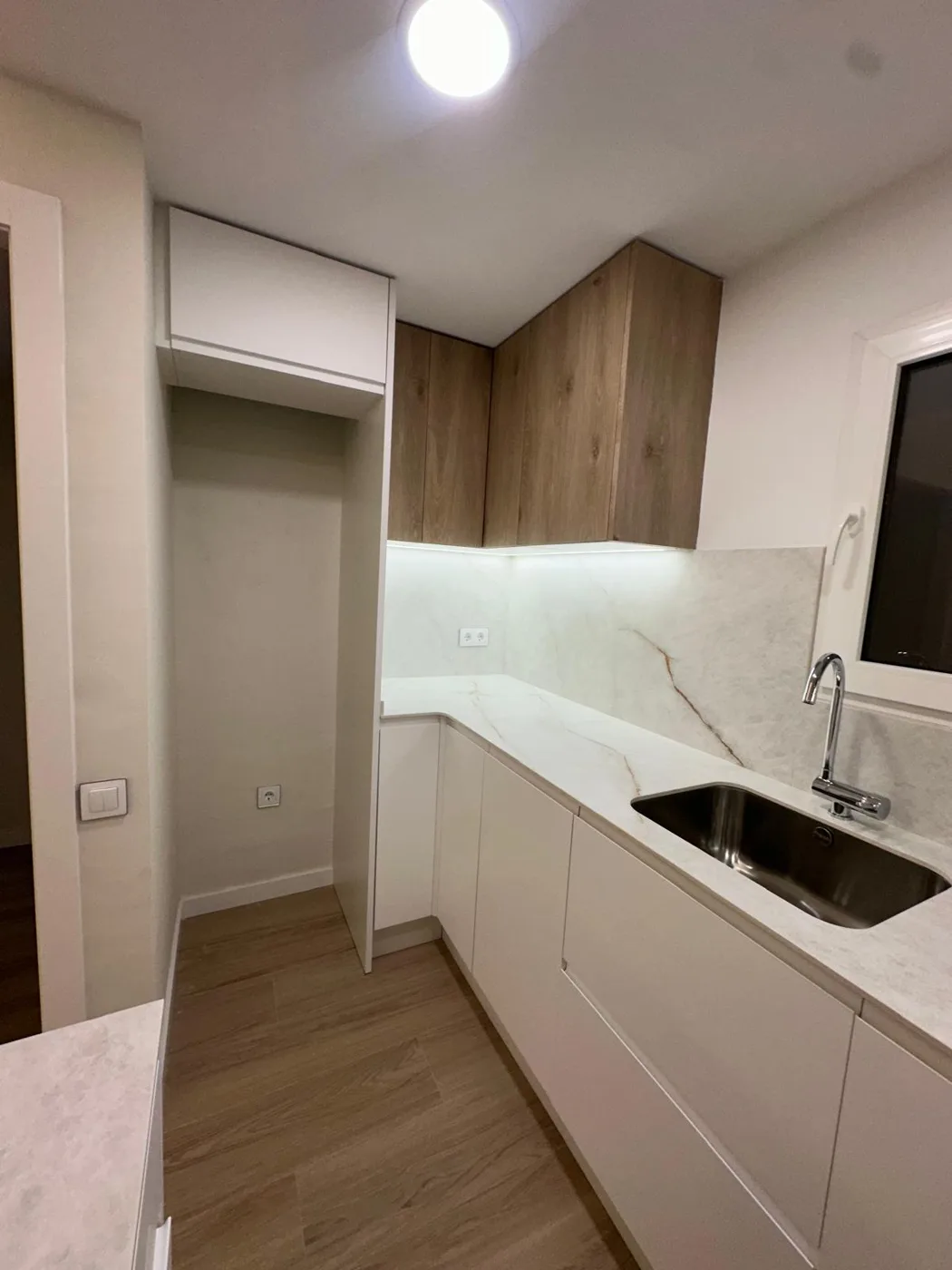 Cocina con muebles blancos y de madera, fregadero y encimera clara